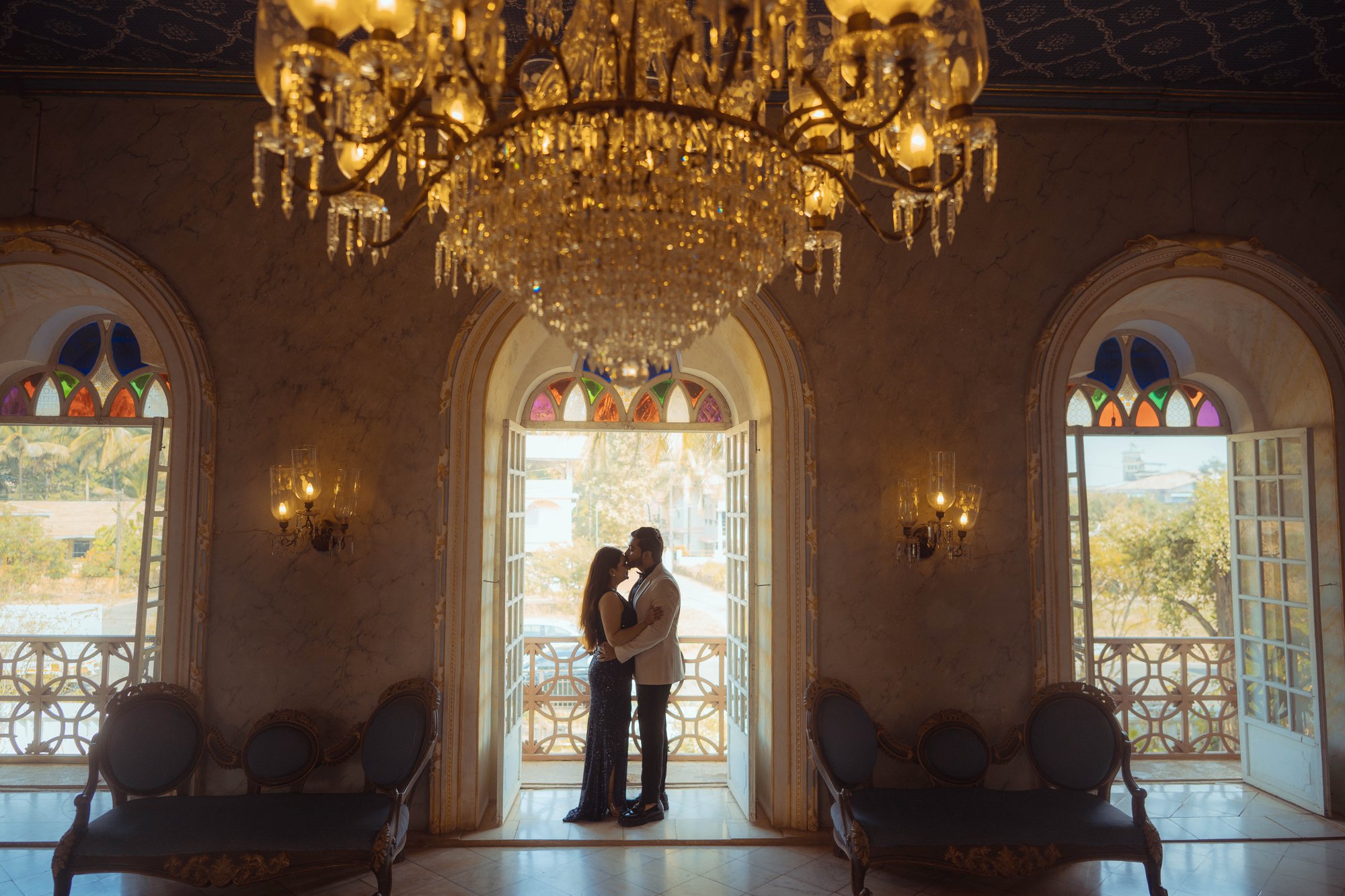 Romantic elegance—bride and groom embrace under a glowing chandelier in a grand hall.